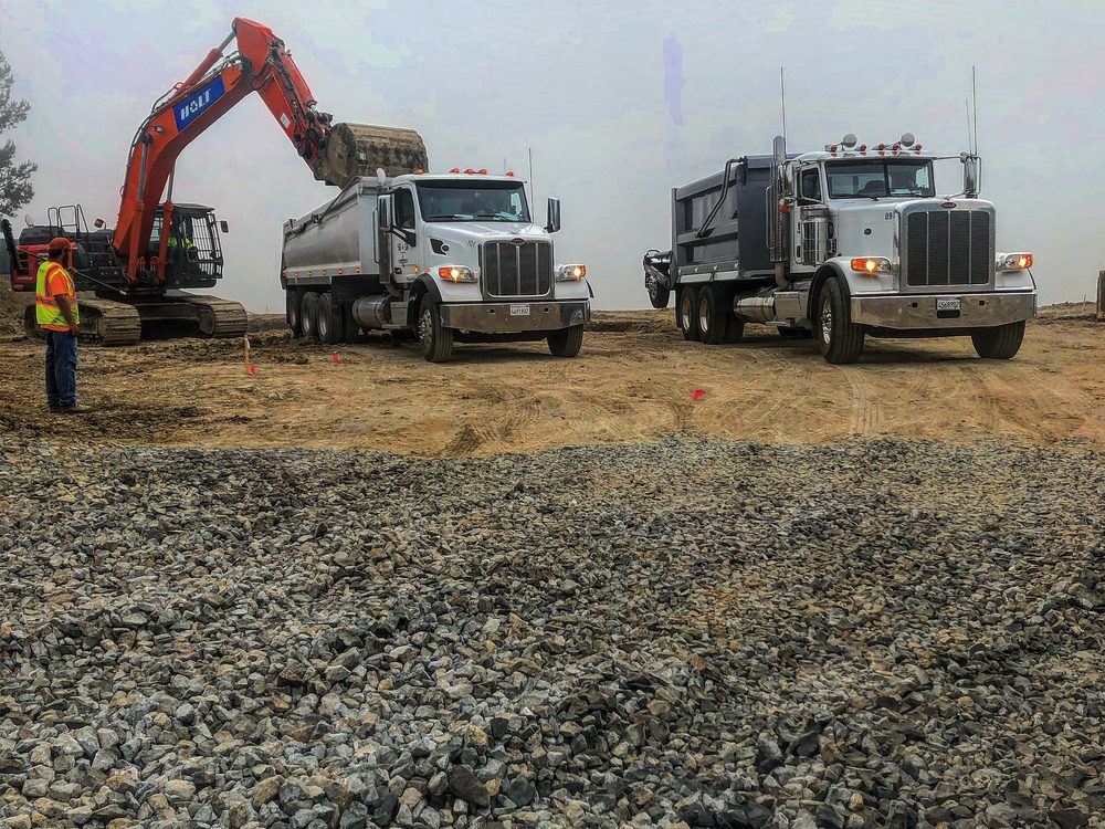 Excavator loading dirt and gravel into B&D Transportation dump trucks